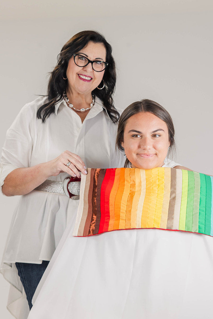 Two women standing inside a boutique, one holding a color analysis fan with various color swatches.