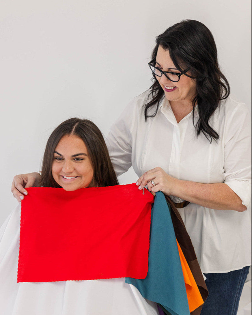Two women standing inside a boutique, one holding a color analysis fan with various color swatches.