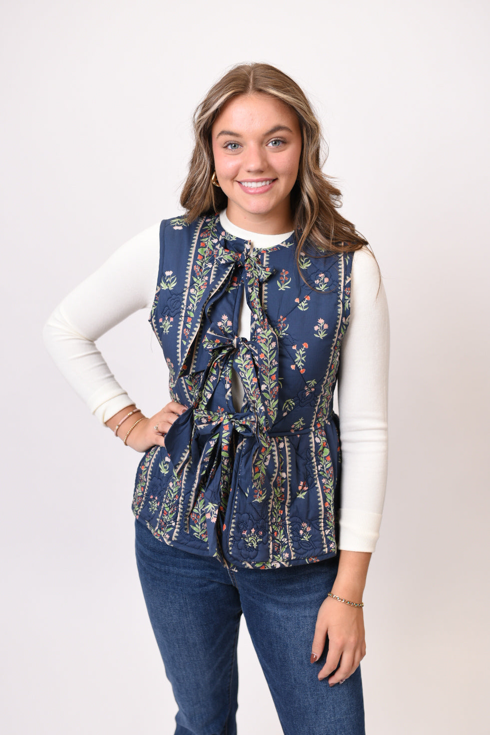 Woman wearing a blue floral vest over a white long-sleeve shirt on a white background