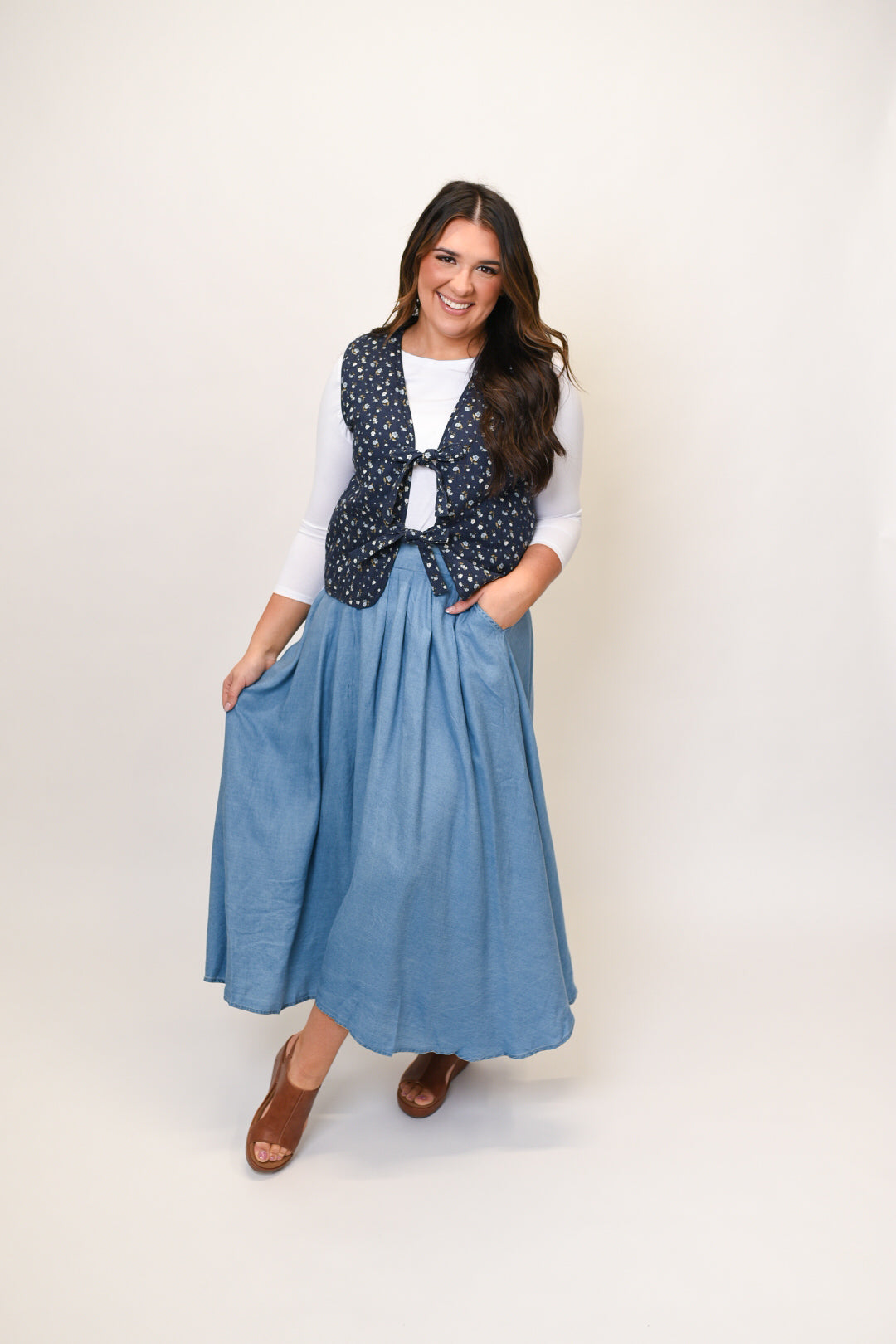 A woman wearing a navy blue quilted vest with a dainty floral print, paired with a white top and a blue skirt.