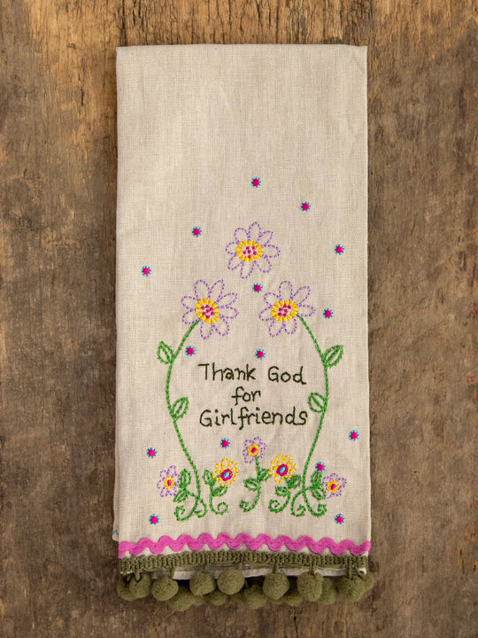 A linen embroidered hand towel with floral patterns and the text 'THANK GOD FOR GIRLFRIENDS' in the center, hanging on a wooden rod.