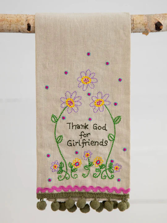 A linen embroidered hand towel with floral patterns and the text 'THANK GOD FOR GIRLFRIENDS' in the center, hanging on a wooden rod.