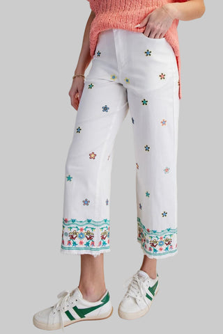 White pants with colorful floral embroidery worn by a person on a beige background