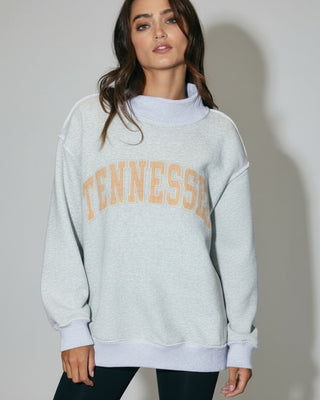 Woman wearing a gray sweatshirt with 'TENNESSEE' printed on it, standing indoors.